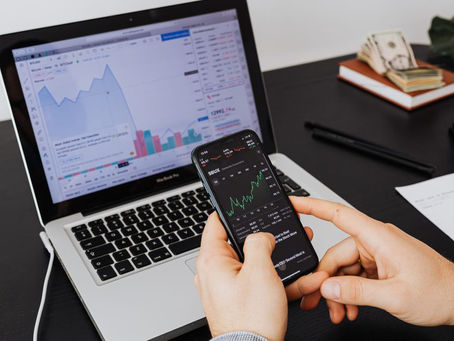 Person analyzing stock market data on a laptop and smartphone indoors.