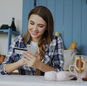 Smiling woman using smartphone and credit card for online shopping in a cozy indoor kitchen.