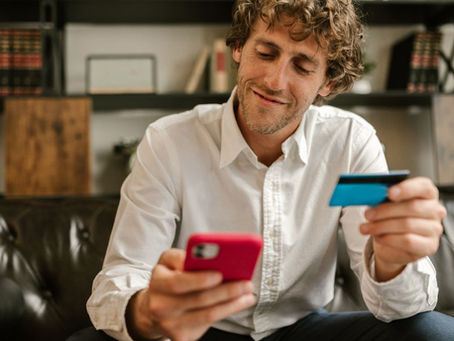 Caucasian man using smartphone and credit card for online shopping indoors.