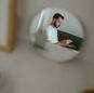 A man reflected in a mirror holding a credit card, engaged in online shopping from his living room.