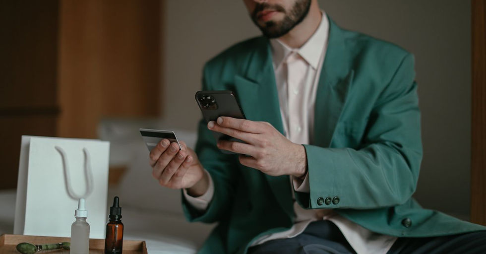 Man using smartphone and credit card for online shopping at home. Teal blazer and home setting create a relaxed feel.