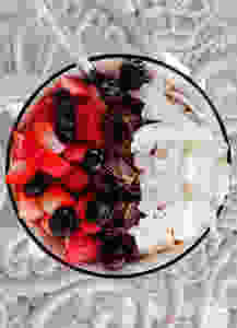 strawberries, blueberries, chocolate and coconut on top of a smoothie bowl on a table