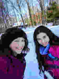 woman and teen girl in winter jackets with background of snowy woods and house in the distance