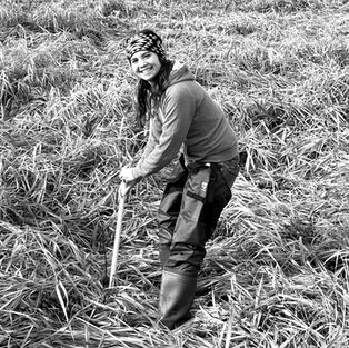 Woman digging in field using a shovel, in tall grass smiling.