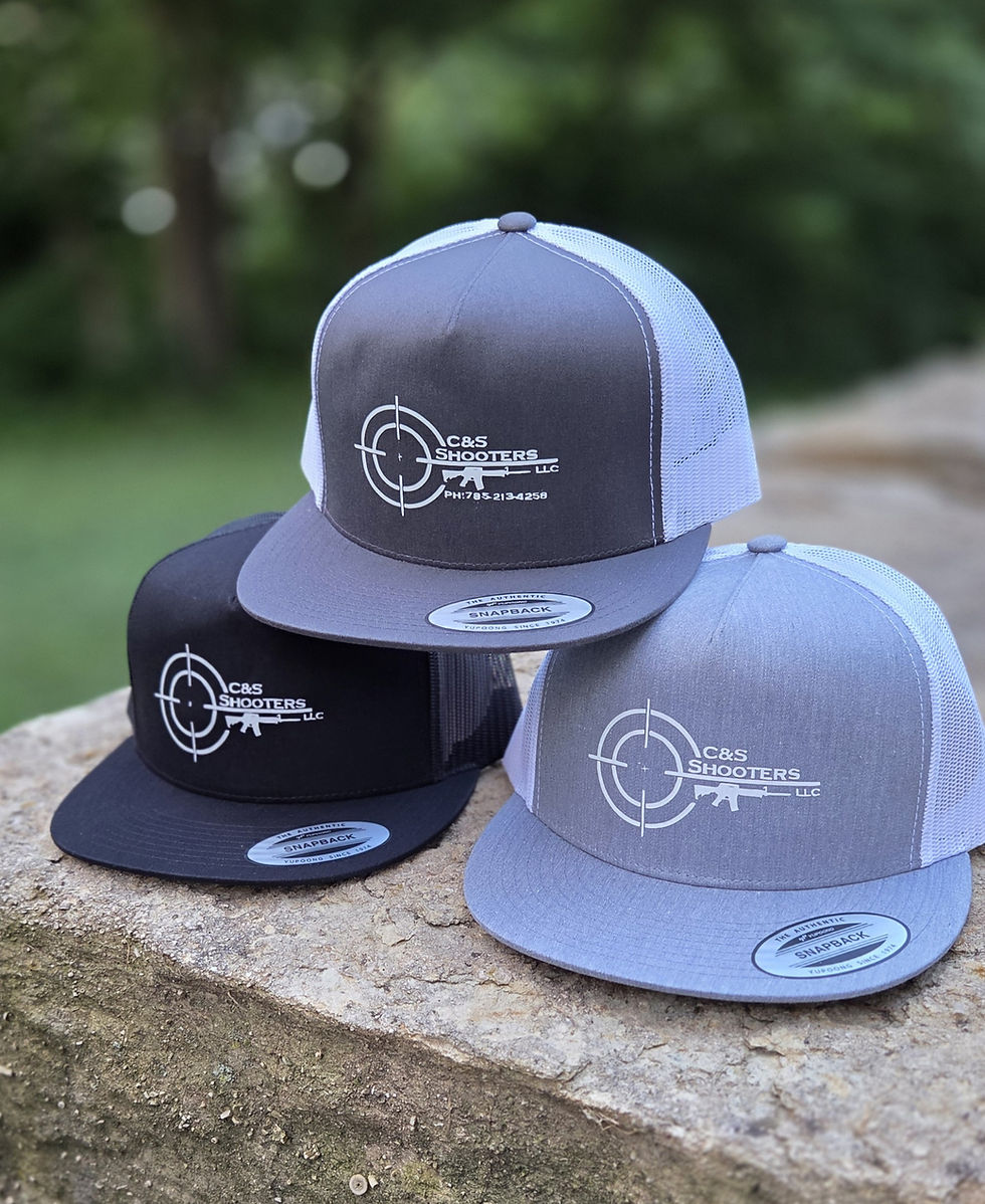 Photo of three C&S Shooters branded snapback hats on a stone surface with a soft green outdoor background, landscape orientation.
