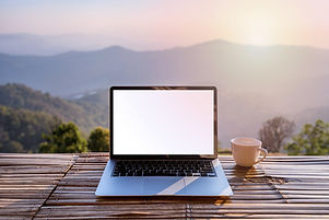Empty screen laptop with cup of coffee and camera with mountain view at sunrise in the mor