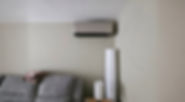 Wall-mounted air conditioner above a grey sofa with folded blankets