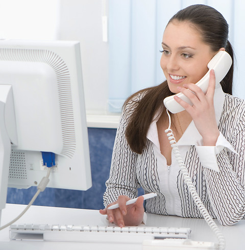 A woman speaks on the phone while working at a computer