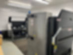 Industrial machines in a well-lit room with white walls. A large machine labeled "FOLEY" is open. Gray and black color scheme.