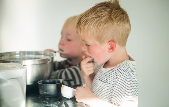 Two toddlers trying new foods in the kitchen
