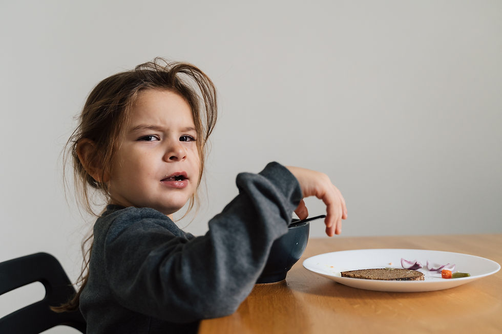 A picky eater girl making an angry face while sitting with a plate of food in front of her