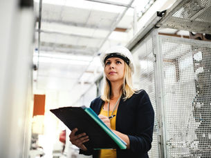 Holding a clipboard with a hardhat in an EV warehouse.