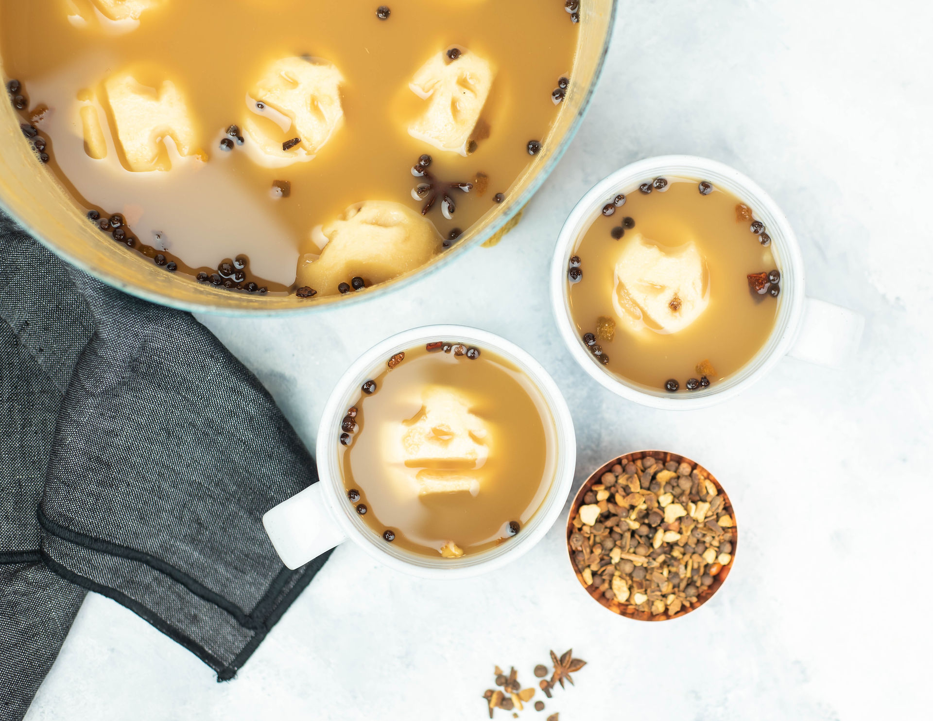 Spooky Skeleton Head Apple Cider in bowl with cups and mulling spices