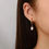 Thumbnail: Woman wearing pearl drop gold huggie earrings
