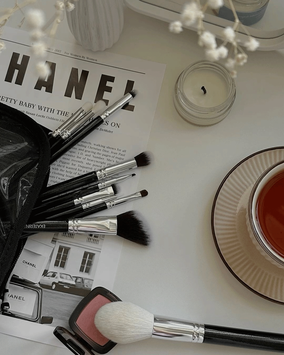 Makeup brushes and candle on white table covering up large of a Chanel magazine