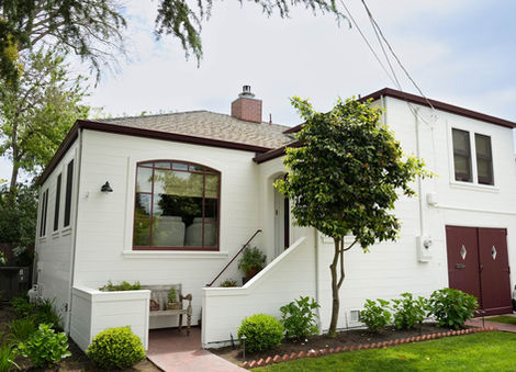 front of white home with red garage door and trim, medium size green tree in font of home and grass. 