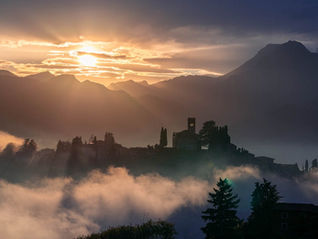 The medieval hill town of Barga rising above morning mist in the Serchio valley at dawn, with the Apuan Alps behind
