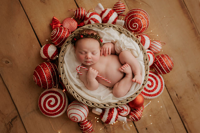 Recién nacido, durmiendo en canasta con adornos navideños rojos y blancos