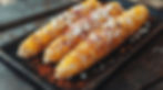 Three grilled corn cobs topped with cheese and chili powder on a black tray, set on a rustic wooden table, creating a tasty, vibrant scene.
