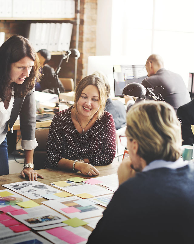 Une manager debout en réunion avec deux collaborateurs donnant des instructions en appliquant les styles de management adaptés à ces deux collaborateurs