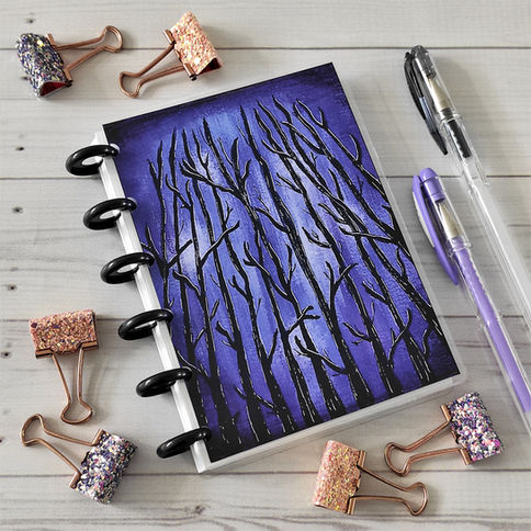 Cuaderno con ramas y clips dorados sobre madera con bolígrafos para escritura.