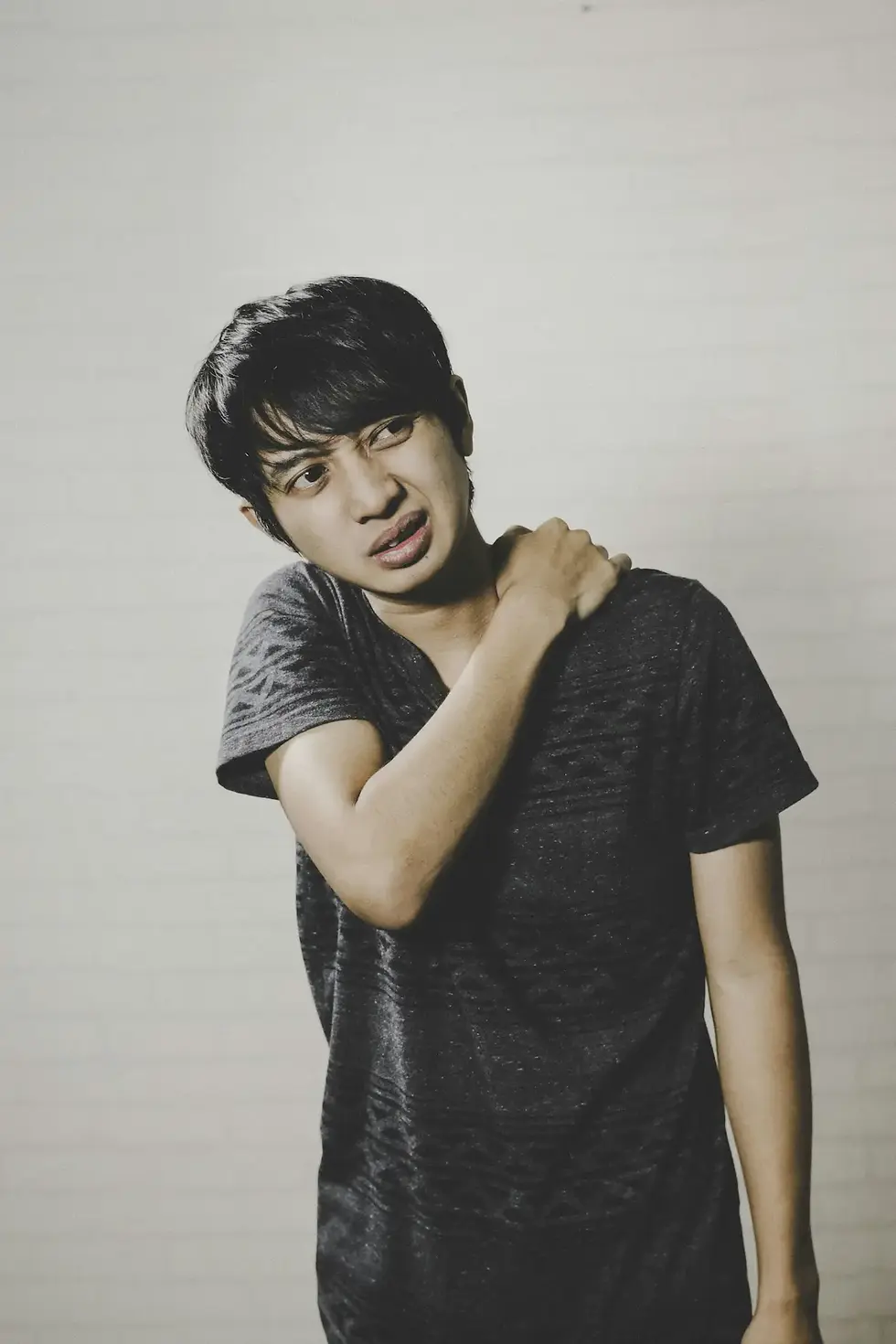 Jeune homme exprimant une douleur entre le cou et l’épaule, douleur cervicale.