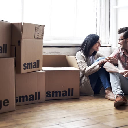 Couple sitting beside moving boxes labeled small while planning their downsizing move.