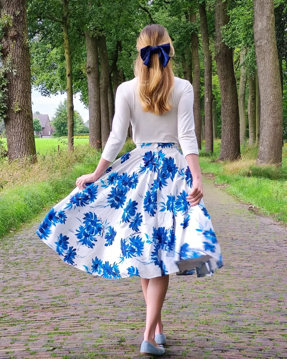 A woman wearing a blue dress and a bow in her hair, walking in the forrest
