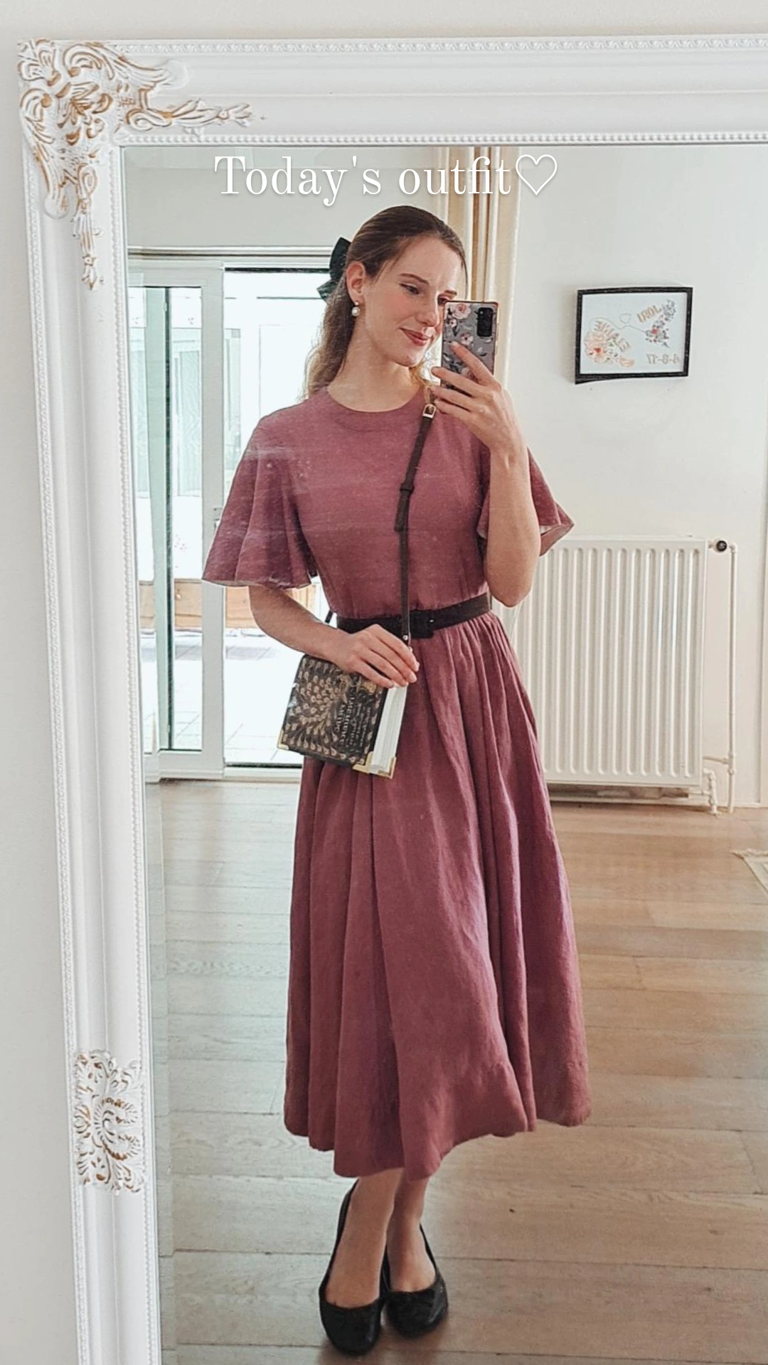 a woman wearing a long purple dress and a green bag, taking a mirror selfie 