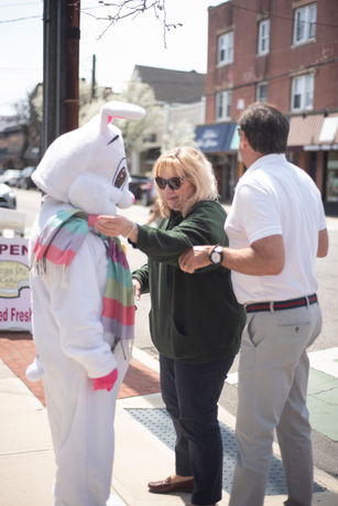 Easter Bunny greets two adults outdoors on a sunny day in Babylon Village.