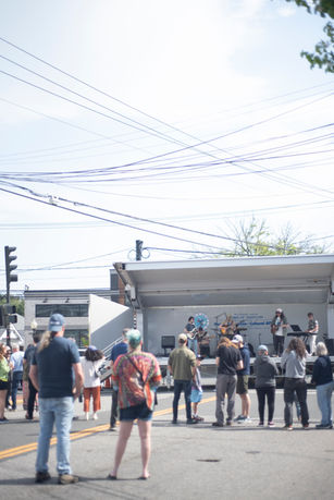 People standing road, some holding signs, near a stage on sunny day