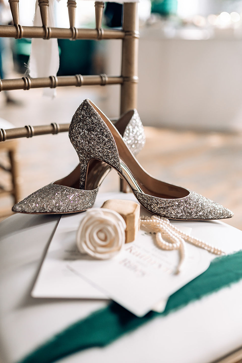 Sparkly heels and a white rose with some stationary on a green-striped chairs.