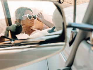 Car mirror showing bride looking into distance with heart sunglasses.