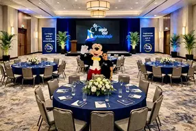 Salón de capacitación empresarial listo para un entrenamiento de cultura de servicio y liderazgo, con mesas redondas, escenario principal y pantalla de La Magia del Aprendizaje.