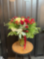 Christmas floral arrangement with red and white roses, winter greenery, berries, and a red ribbon displayed in a clear vase