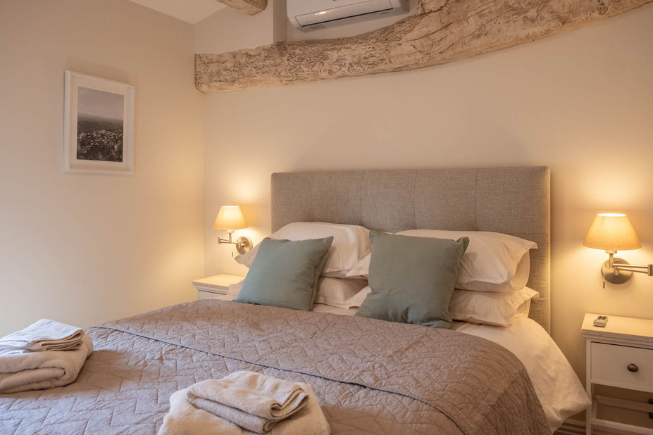 Master bedroom at La Borgada Penthouse with a double bed, neutral Provençal décor, and views of Saint Gregiore church