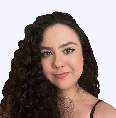 Mulher branca, de cabelos pretos e cacheados. Está olhando para a câmera, com um sorriso contido e expressão mais séria. A foto possui fundo branco.