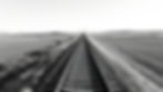 black and white railroad tracks going across a landscape from left to right on rolling hil