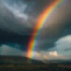 Vibrant rainbow arching across a cloudy, rainy sky.