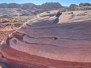 Rocky desert landscape at Valley of Fire State Park in Nevada with layered red and pink sandstone formations under a clear blue sky. Rugged hills in the background.
