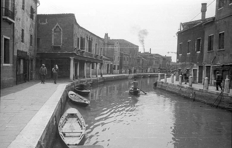 Black and white photo of a Murano canal in 1932: rowing boats, quays, houses and smoke from a furnace chimney