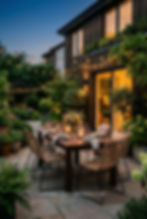 Outdoor dining setup with candles and string lights on a patio at dusk, surrounded by greenery. Cozy, inviting atmosphere.