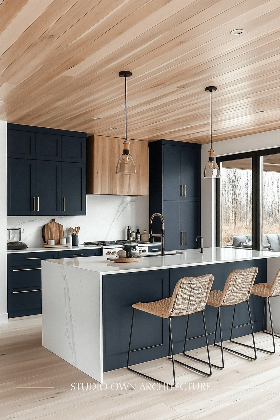 Modern kitchen with navy cabinets, white island, wicker chairs, and wood ceiling. Large windows show a natural landscape.