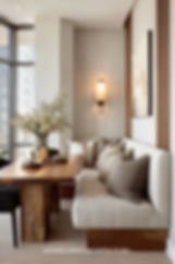 Cozy dining nook with beige cushions, wooden table, and floral centerpiece. Wall art and sconce light create a warm, inviting atmosphere.