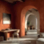 Cozy room with terracotta walls, wooden desk, chair, and archways. Potted plants and soft lighting create a warm, serene atmosphere.