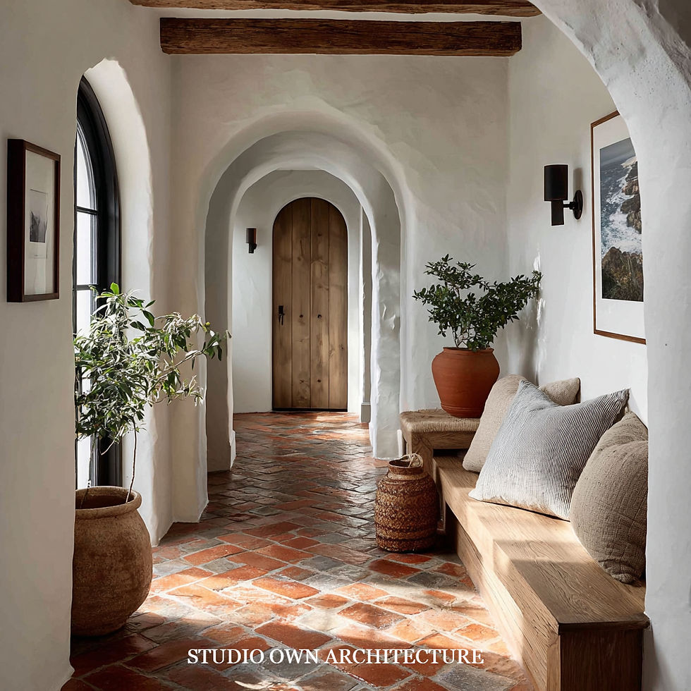 Rustic hallway with terracotta tiles, arched wooden door, and white walls. Wooden bench with cushions, potted plants, and framed art.