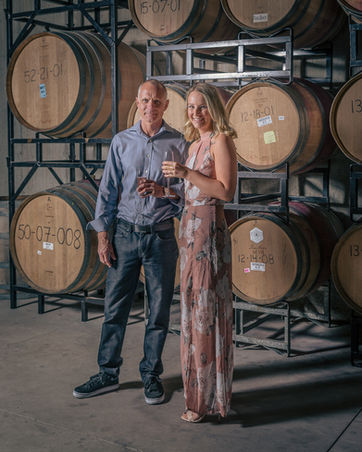 Couple holding wine in front of wine barrel wall