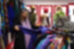 Customers shopping in the Secondhand Circus location with one individual expressing extreme happiness at her unique vintage clothing find, showcasing the unique design and branding of the in-person retail store. You can see the selection of unique vintage clothes, upcycled clothes, and unique accessories and decor.