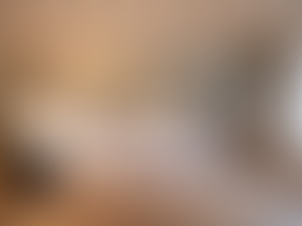 Spacious bedroom at Lunaria Suites in Florence featuring a perfectly made hotel-style bed with crisp white linens, decorative cushions, and a textured green throw. The room is bathed in soft natural light from large windows with sheer curtains, complemented by warm bedside lamps, exposed wooden beams, pale sage walls, and elegant contemporary furnishings.