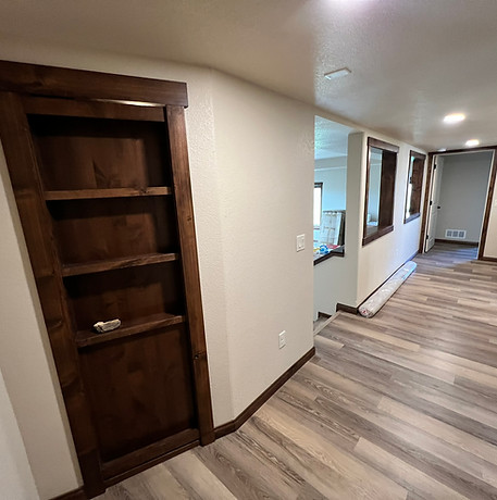 Finished basement hallway with wood trim, vinyl plank flooring, and a built-in hidden bookcase door
